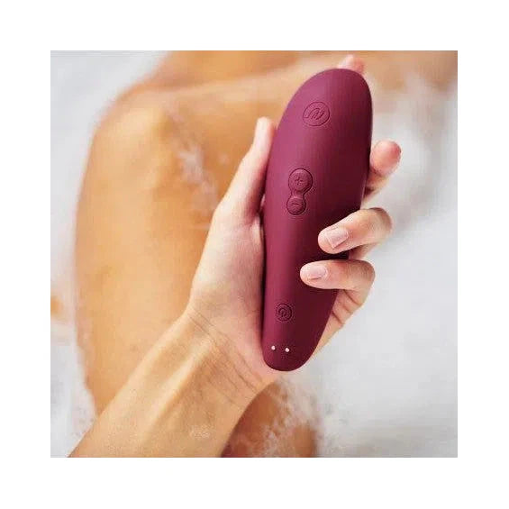 Main qui tient un sextoy clitoridien à air pulsée Classic 2 violet de Womanizer dans un bain