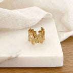 Instants Plaisirs – Bague Fei - Acier, bague dorée en forme de feuilles, posée sur un support blanc