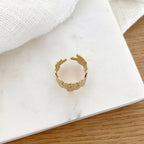 Instants Plaisirs – Bague Fei - Acier, bague dorée à motifs floraux sur un fond blanc marbré