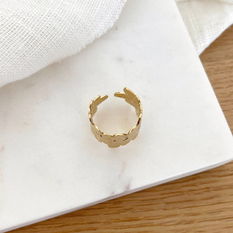 Instants Plaisirs – Bague Fei - Acier, bague dorée à motifs floraux sur un fond blanc marbré