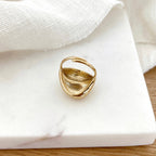 Instants Plaisirs – Bague Dody - Acier, bague dorée brillante posée sur une surface en marbre blanc