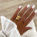Instants Plaisirs – Bague Dody - Acier, bague dorée portée sur une main aux ongles blancs, chemise blanche